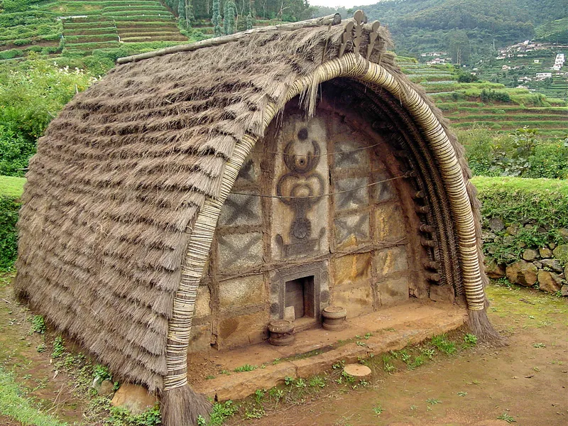 Toda people standing behind a traditional Toda hut in the Nilgiris, showcasing their rich tribal heritage, unique architecture, and cultural legacy.